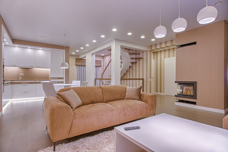 Interior scene showing a white fabric-covered sofa positioned against a plain, light-colored wall. To the right of the sofa, there are three cardboard boxes of varying sizes stacked on top of each oth